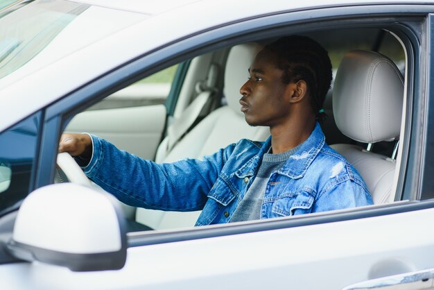 A young dark-skinned man sitting in a car in a white T-shirt