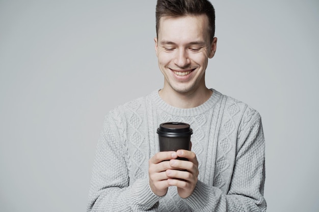 A young darkhaired student holding a black cup of coffee a\
satisfied expression on his face