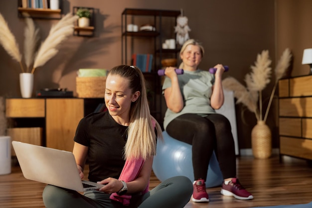 Photo young daughter sits on mat looking for warming upexercises in laptop while charming