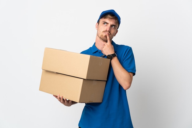 Young delivery blonde man isolated on white having doubts while looking up