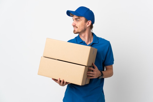 Young delivery blonde man isolated on white wall looking side