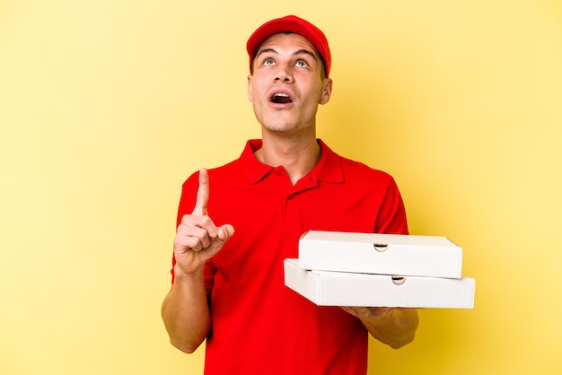 사진 열린 입으로 거꾸로 가리키는 노란색 배경에 고립 된 피자를 들고 젊은 배달 백인 남자.