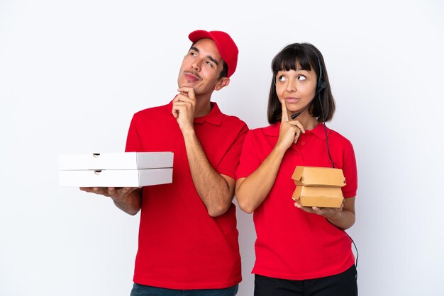 Молодая пара курьеров держит пиццу и гамбургеры на белом фоне, думая об идее, глядя вверх