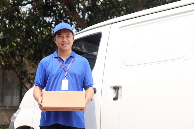 Young Delivery Man in Blue Uniform Carrying Cardboard Box Beside Of Truck.