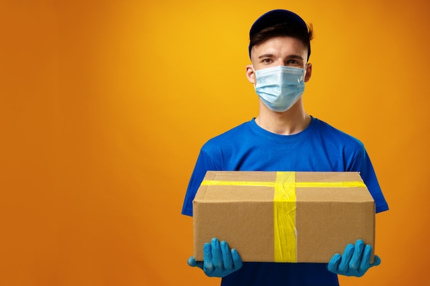 Photo young delivery man in face mask and gloves holding cardboard box parcel