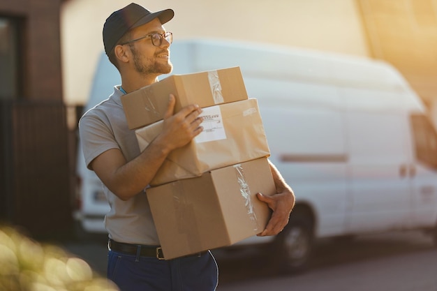 young delivery man holding stack of packages while making home delivery at residential district