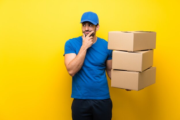 Young delivery man over isolated yellow wall thinking an idea