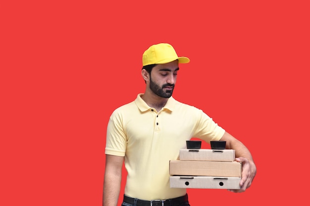 young delivery man looking infront in yellow tshirt holding 3 pizza boxes indian pakistani model