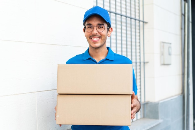 Young delivery man at outdoors holding boxes with happy expression