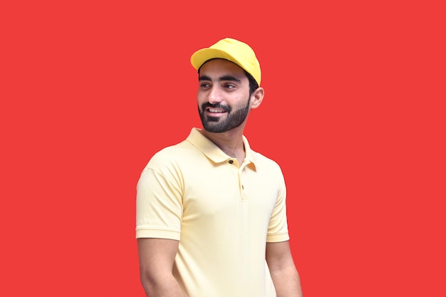 young delivery man side pose with smile in yellow t shirt over red background indian pakistani model