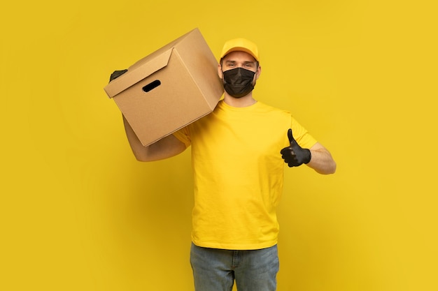 Young delivery man in yellow tshirt, mask, gloves with box isolated