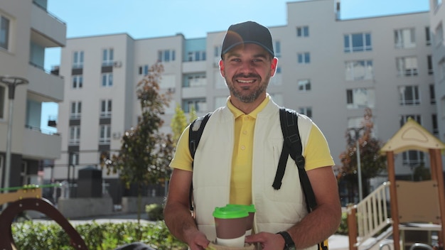 Young delivery man in yellow uniform with takeaway coffee\
looking at camera and smile and waiting for customer delivery\
service takeaway orders