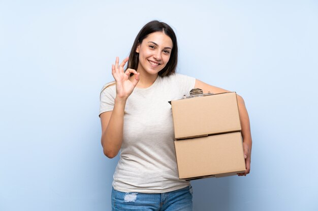 Young delivery woman over blue brick wall showing ok sign with fingers