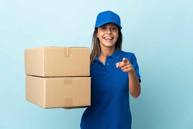 Young delivery woman isolated on blue wall surprised and pointing front
