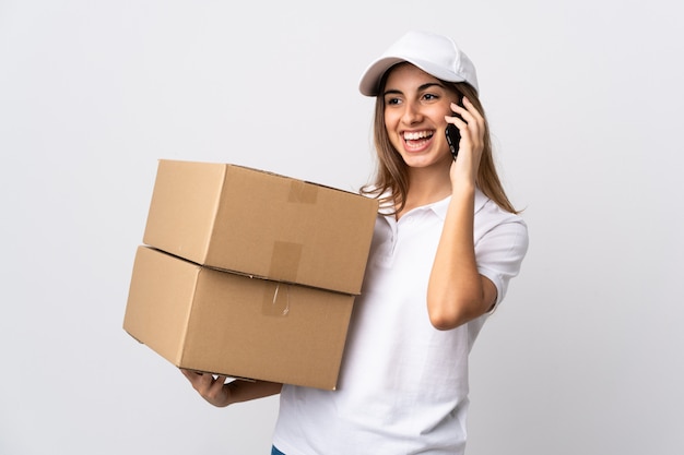 Young delivery woman over isolated white wall keeping a conversation with the mobile phone with someone