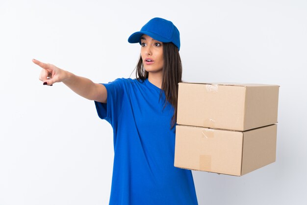 Young delivery woman over isolated white wall pointing away