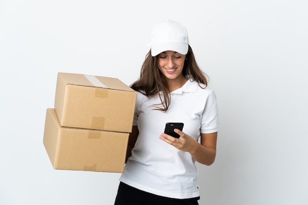 Young delivery woman over isolated white wall sending a message with the mobile