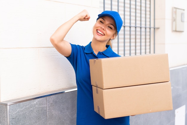 Young delivery woman at outdoors holding boxes and celebrating a victory