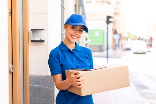 Young delivery woman at outdoors holding boxes and a tablet with happy expression