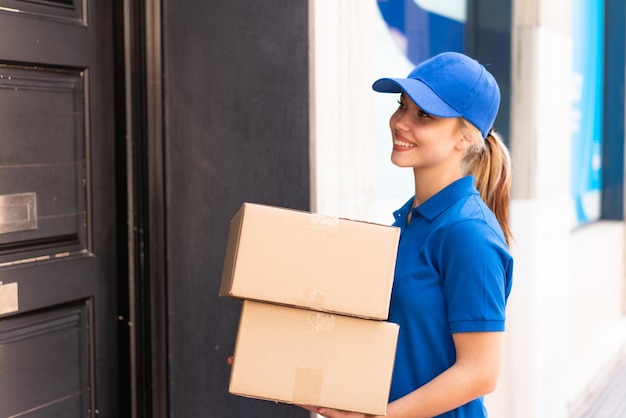 Young delivery woman at outdoors holding boxes with happy expression