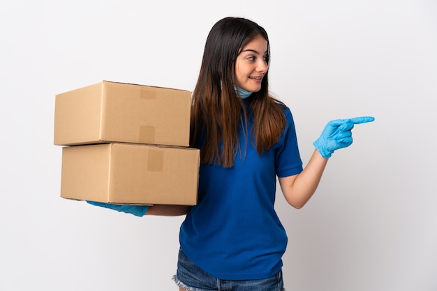 Young delivery woman protecting from the coronavirus with a mask isolated on white pointing to the side to present a product