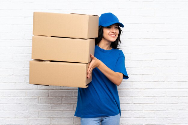 Young delivery woman over white brick wall