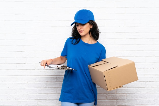 Young delivery woman over white brick wall