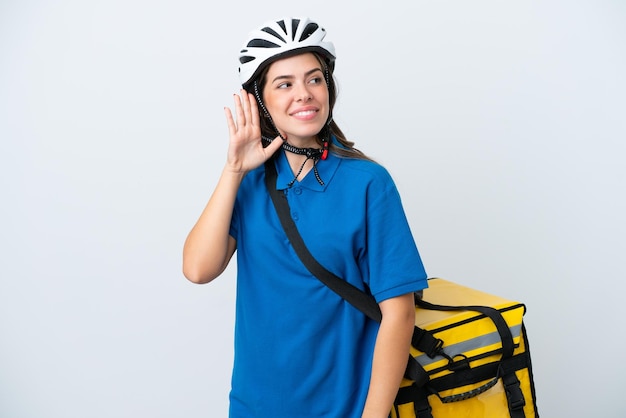 Young delivery woman with thermal backpack isolated on white background listening to something by putting hand on the ear