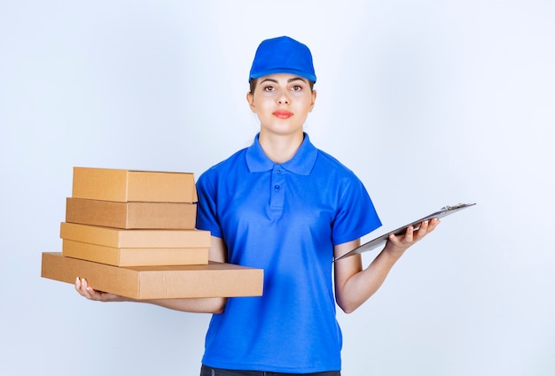 Young deliverywoman in blue uniform holding cardboard boxes and clipboard.