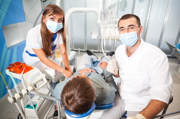 Giovane uomo del medico dentista in uniforme bianca e maschera speciale e paziente d'esame dell'uomo della giovane donna dell'infermiera in studio dentistico