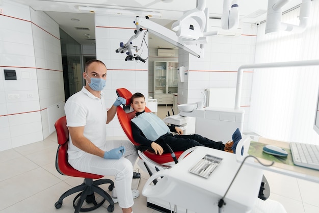 Un giovane dentista esamina e tratta i denti di un bambino di otto anni in un moderno primo piano di odontoiatria bianca trattamento di protesi dentarie e sbiancamento dei denti odontoiatria moderna prevenzione