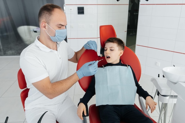 젊은 치과 의사는 현대 흰색 치과 근접 촬영에서 8세 소년의 치아를 검사하고 치료합니다. 치과 보철 치료 및 치아 미백 현대 치과 예방