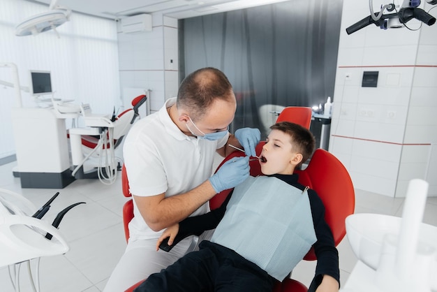 젊은 치과 의사는 현대 흰색 치과 근접 촬영에서 8세 소년의 치아를 검사하고 치료합니다. 치과 보철 치료 및 치아 미백 현대 치과 예방