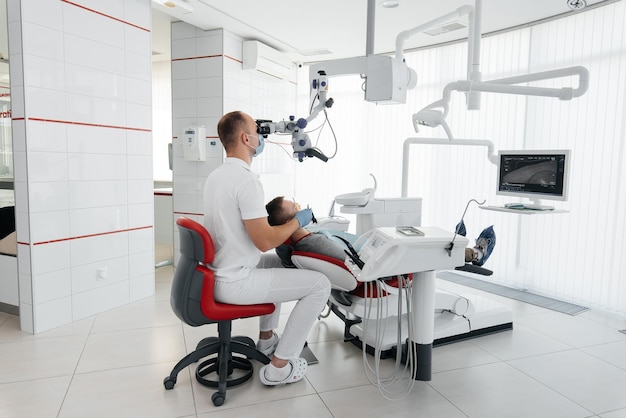 A young dentist examines and treats the teeth of a young guy in modern white dentistry using a microscope Dental prosthetics treatment and teeth whitening Prevention of caries