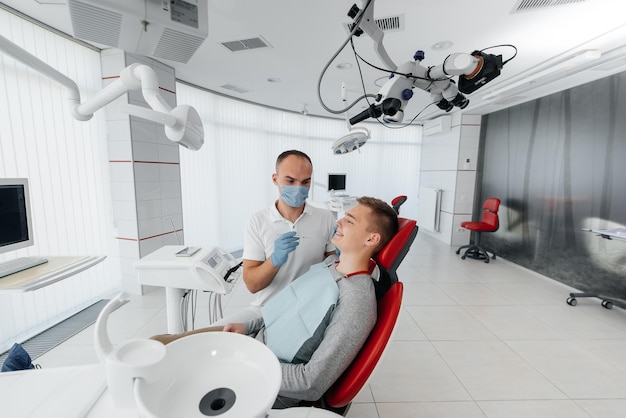 A young dentist examines and treats the teeth of a young man in\
modern white dentistry closeup dental prosthetics treatment and\
teeth whitening modern dentistry prevention