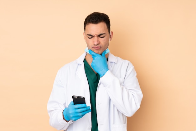 Young dentist man holding tools on beige wall thinking and sending a message