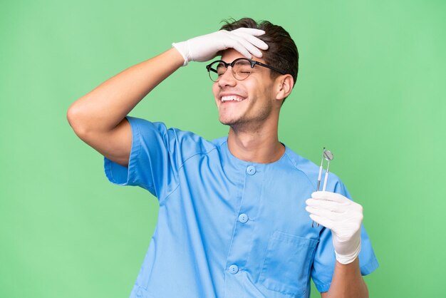 Young dentist man holding tools over isolated background smiling a lot