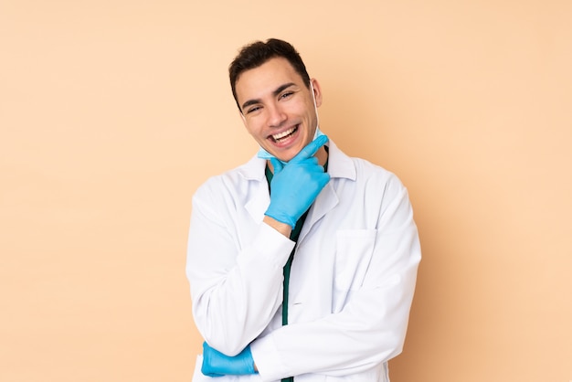Молодой стоматолог мужчина держит инструменты, изолированные на бежевой стене улыбается