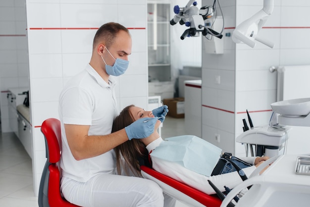 A young dentist specialist examines and treats the teeth of a beautiful woman in modern white dentistry Dental prosthetics treatment and teeth whitening Modern dentistry