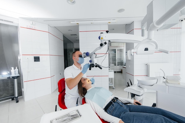 A young dentist specialist examines and treats the teeth of a beautiful woman in modern white dentistry using a microscope Dental prosthetics treatment and teeth whitening