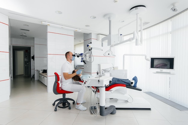 A young dentist specialist examines and treats the teeth of a beautiful woman in modern white dentistry using a microscope Dental prosthetics treatment and teeth whitening