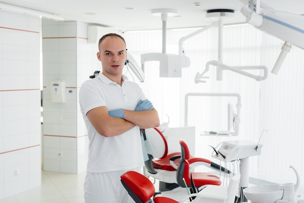 A young dentist stands near a red dental chair and smiles in modern white dentistry Treatment and prevention of caries from youth Modern dentistry and prosthetics