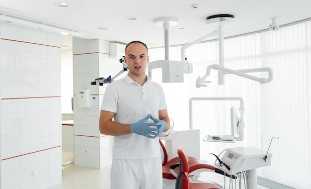 A young dentist stands near a red dental chair and smiles in modern white dentistry Treatment and prevention of caries from youth Modern dentistry and prosthetics