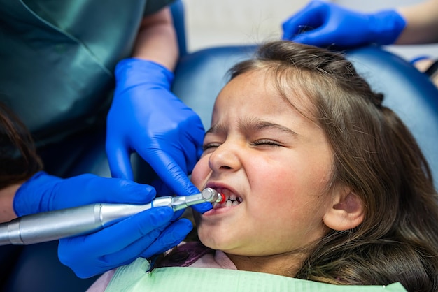Молодая дантистка чистит зубы маленькой девочке Концепция чистки зубов у ребенка