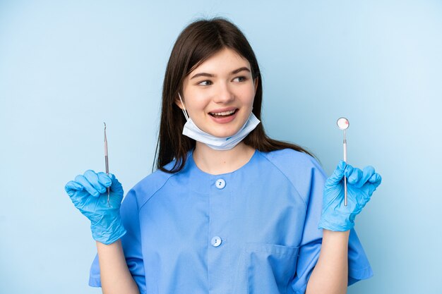 Young dentist woman holding tools over isolated blue wall
