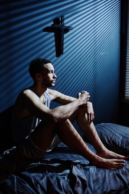 Young depressed man sitting on bed while staying awake till morning