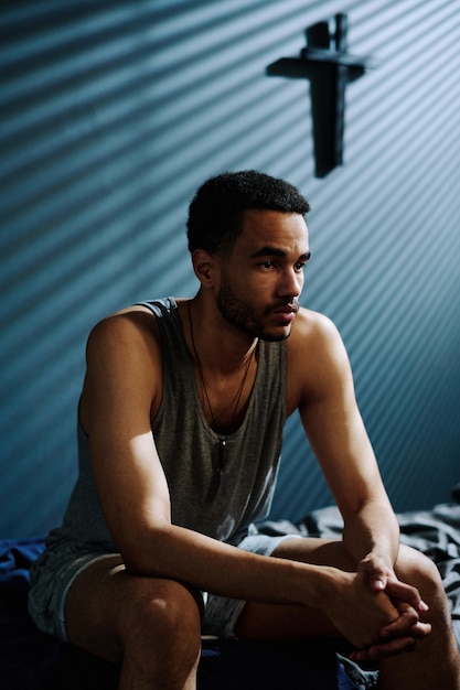 Young depressed man with post traumatic syndrome sitting on bed at night