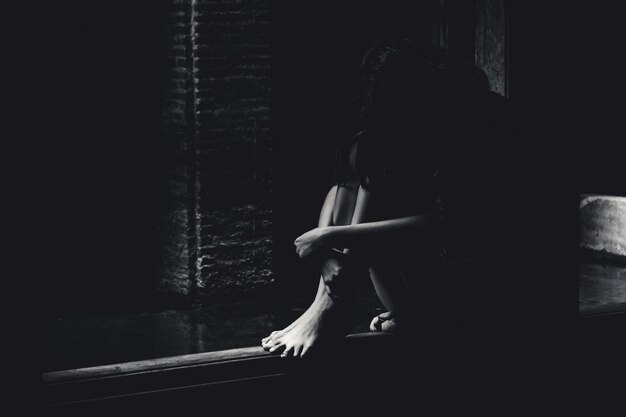 Фото Молодая депрессивная женщина сидит в темной комнате.