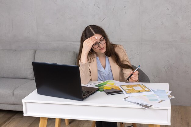 A young designer girl sitting at a table draws on a tablet. Makes business calculations on the computer.