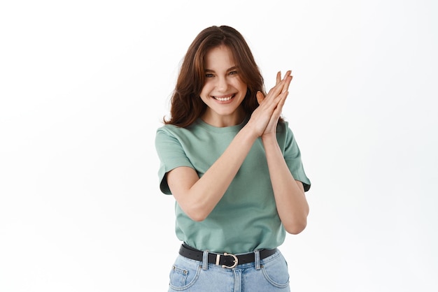 Фото Молодая решительная девушка улыбается и потирает руки, наслаждаясь хорошей возможностью, готовой к работе, стоя оптимистично и уверенно на белом фоне